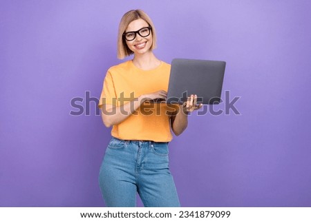 Photo of adorable good mood woman with bob hairstyle wear yellow t-shirt in eyewear holding laptop isolated on purple color background