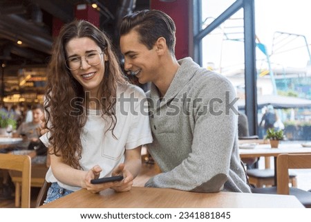 A Smiling young couple sitting at coffee shop looking at mobile phone.