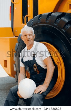 Happy Industrial worker male senior in helmet on background of production of excavator, working on industry factory.