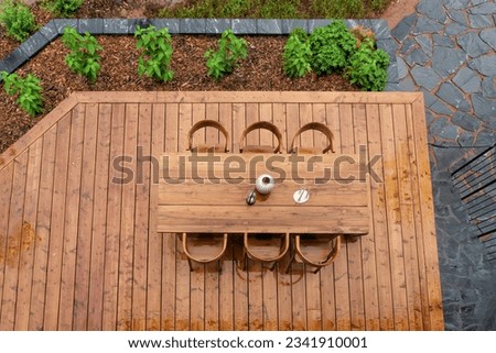 A stunning wooden terrace table group, seen from top to bottom. Beautiful wooden terrace bordered with plants after the rain.