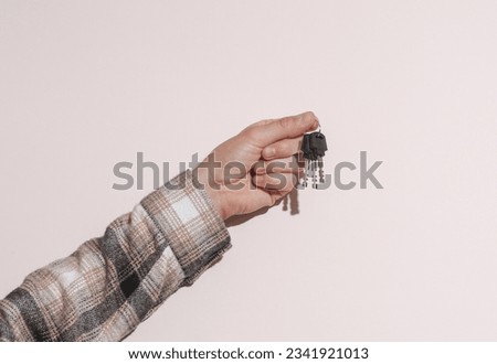 Man's hand in shirt holding keys on beige background with shadow