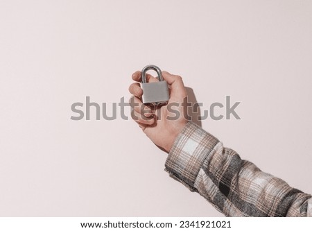 Man's hand in shirt holding metal lock on beige background with shadow