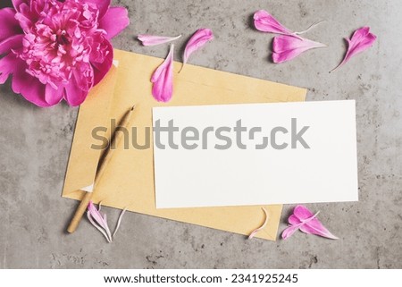 Invitation or greeting card mockup, envelope with peony petals on a concrete background. Top view, copy space.