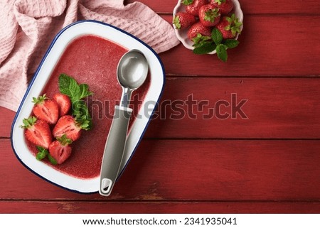 Strawberry granita or fresh berry sorbet in white rustic bowl on old wooden table background. Ice cream with strawberry and mint. Summer treat. Top view.