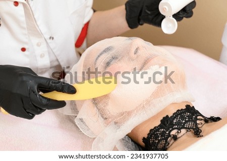 A beautician uses a spatula to apply cream to an already prepared face with gauze, a procedure for facial skin with couperosis. Royalty-Free Stock Photo #2341937705