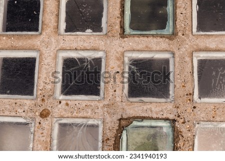 A close up detailed photo of intact and damaged glass blocks installed into rectangular concrete plate in the pavement to let natural light into the cellar room.