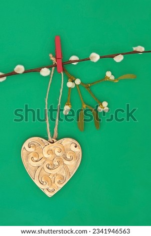 Gold heart shaped christmas bauble with mistletoe over green paper background.