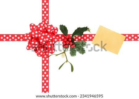 Christmas gift box with red polka dot ribbon and bow, gift tag, holly, fir leaf sprig and mistletoe over white background.