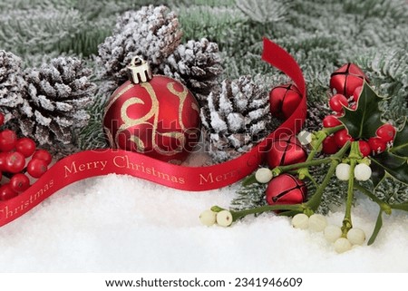 Merry christmas ribbon on snow with red bauble and bell decorations, fir, holly, mistletoe and pine cones.