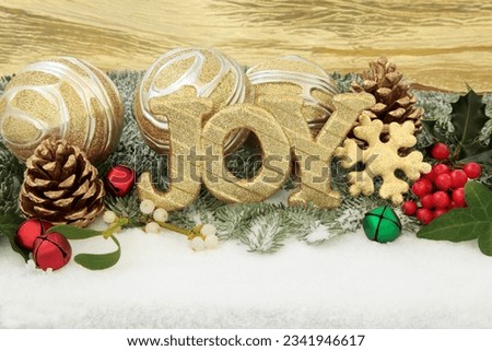 Christmas joy sign with gold bauble decorations, holly and winter greenery over snow background.