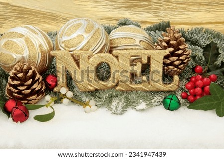 Christmas noel sign with gold bauble decorations, holly and winter greenery over snow background.