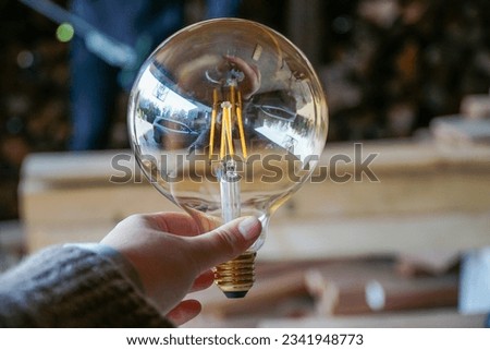Building Ideas: A hand holding a light bulb against a backdrop of wood and construction, symbolizing innovation in progress.