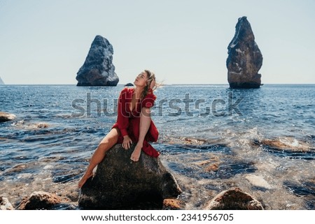 Woman summer travel sea. Happy tourist in long red dress enjoy taking picture outdoors for memories. Woman traveler posing on beach at sea surrounded by volcanic mountains, sharing travel adventure