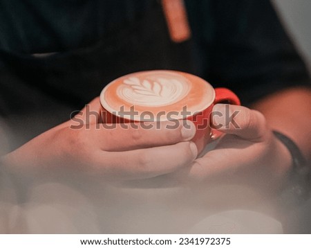 Someone is holding a cup of coffee with a picture of flowers. Coffee. Cup. Milk. Full cream. Barista. Hand. Cappuccino. Coffeeshop. Coffee Latte. Hot. Hot coffee. Photography. Aesthetic. Vintage.