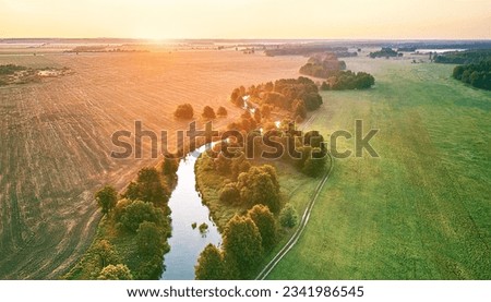 Aerial summer sunrise view. Rural landscape, river meandering in forest green trees. Morning Misty Scene. Serene atmosphere fog panorama. Agriculture fields, wood on riverbank. Beauty of nature