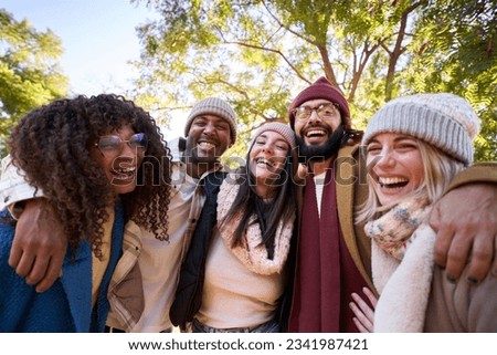 Group multi-ethnic friends posing laughing outdoor winter portrait. Young people hugging together look smiling at camera holiday photo in park on sunny day. Friendship relationships millennial.