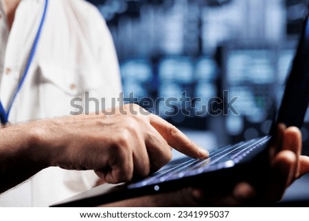 Overseeing manager using laptop to examine blade servers for power fluctuations, close up. Experienced supervisor monitoring high tech data center systems, identifying potential malfunctions Royalty-Free Stock Photo #2341995037