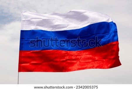 Close-up picture of national flag of Russian Federation waved in breeze on white clouded sky background.