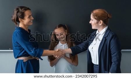 The teacher shakes hands with the mother of the schoolgirl standing at the blackboard.  Royalty-Free Stock Photo #2342007295