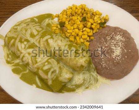 Two green sauce enchiladas with refried beans and sauté corn on the side served on a white plate.