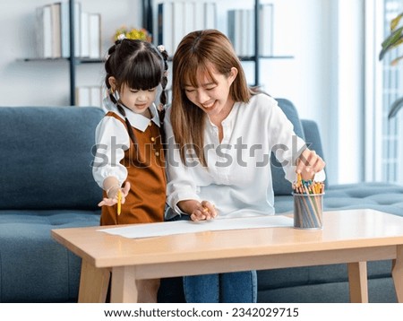 Millennial Asian cheerful happy young beautiful female teenager mother nanny babysitter sitting smiling holding color pencils drawing painting together with little cute preschooler daughter girl. Royalty-Free Stock Photo #2342029715