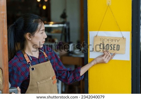 Close-up shot of beautiful Asian woman breakfast of cafe Changing the storefront sign to say store is closing. Woman's hand holding wooden signboard with text CLOSED Stuck in front of coffee shop door