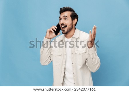 Portrait of a brunette man talking on the phone mobile and internet online, smile with teeth surprise and happiness, on a blue background in a white T-shirt, copy space 