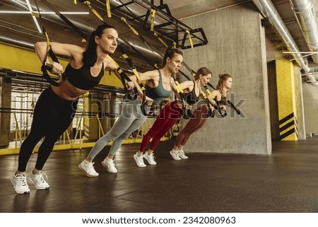 Fit young women doing push-ups training exercises with fitness trx suspension straps at gym
