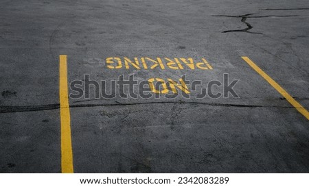 No Parking Sign on the road. Yellow no parking lines on fresh road. No parking signage on a concrete floor. No parking text written and white line with broken cement wall, sign word on street. 