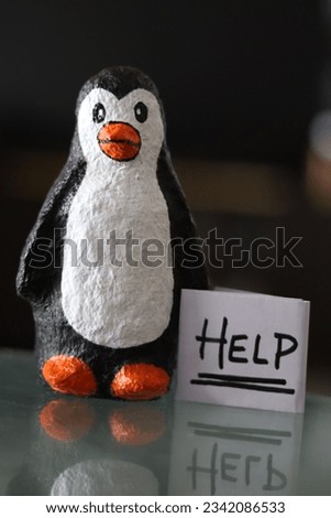 A baby Penguin made with paper mache holding a paper Sign of Help in the side with bokeh