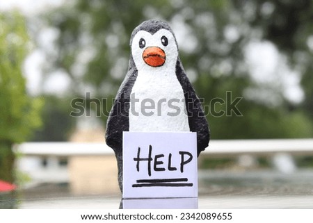 A baby Penguin made with paper mache holding a paper Sign of Help in the front with bright green bokeh
