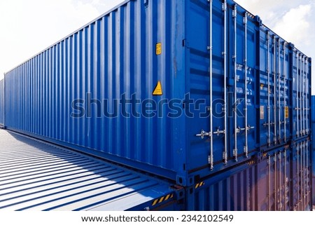 Blue cargo containers are stacked in the storage area under bright cloudy sky