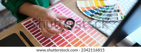 Designer with magnifying glass works with pantone scale in art studio. Computer, drawing tablet, lens and manager woman hands on office desk, top view. Royalty-Free Stock Photo #2342116815
