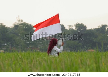 Asian woman in white shirt waving Indonesian flag excitedly in rice field