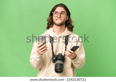 Young photographer man over isolated background holding coffee to take away and a mobile while thinking something