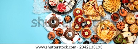Fun Halloween dinner party table scene on a blue background. Top view. Pizza, pie, spaghetti and snacks. Panorama with copy space.
