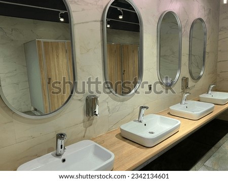 Modern restroom interior with stone gray tiles. Contemporary interior of public toilet. minimal interior with white tiles, round mirrors. Perspective of men's restroom. commercial bathroom.  Royalty-Free Stock Photo #2342134601