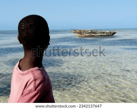 African adolescent boy looking out to sea at a traditional ,wooden ngalawa boat at low tide , Jambiani, Zanzibar. High quality photo