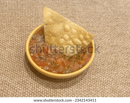 A small bowl with fresh Mexican salsa and a corn tortilla chip.