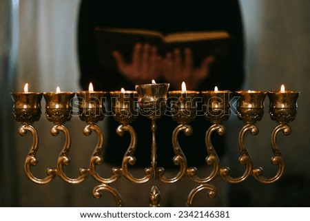 hanukkah candle holder with lighted candles and man with a torah book in hands