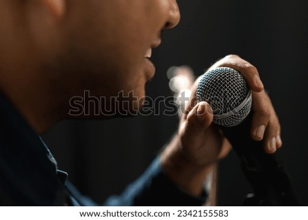 Attractive singer man singing music and playing guitar on stage with spotlight strike through the darkness at concert event. Musician performing live with light and smoke at hall. Royalty-Free Stock Photo #2342155583