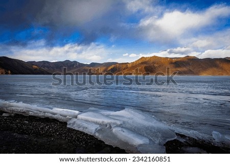 A winter scene unfolds at Pangong Lake, Ladakh, as ice plates stack up along the serene shoreline, offering a mesmerizing sight under the soft glow of the blue hour