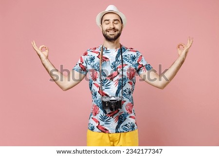 Smiling young traveler tourist man in summer clothes hat photo camera hold hands in yoga gesture meditating isolated on pink background. Passenger traveling on weekends. Air flight journey concept