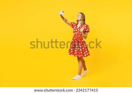 Full body young woman she wear red dress casual clothes doing selfie shot on mobile cell phone post photo on social network waving hand isolated on plain yellow background studio. Lifestyle concept