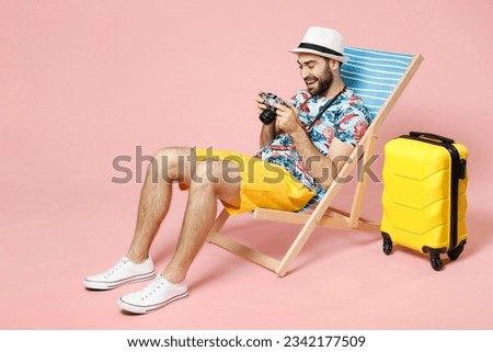 Full length funny traveler tourist man in summer clothes hat sit on deck chair hold retro vintage photo camera isolated on pink background. Passenger traveling on weekend. Air flight journey concept Royalty-Free Stock Photo #2342177509