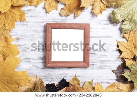 Blank rectangular photo frame lies on vintage wooden desk with bright autumn foliage. Flat lay with autumn leaves on white wooden surface. Simple brown picture frame with copy space for design.