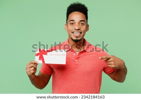 Young man of African American ethnicity he wear pink t-shirt hold point finger on gift certificate coupon voucher card for store isolated on plain green background studio portrait. Lifestyle concept