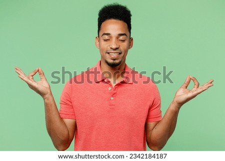 Young tranquil spiritual man of African American ethnicity he wearing pink t-shirt hold spread hands in yoga om aum gesture relax meditate try to calm down isolated on plain pastel green background