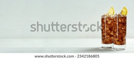 Tasty refreshing soda drink with ice cubes and lemon slices on white wooden table. Banner design with space for text