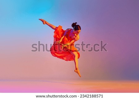Dynamic image of artistic young woman dancing in elegant red dress against gradient multicolor background in neon light. Concept of modern dance style, hobby, art, performance, lifestyle, ad